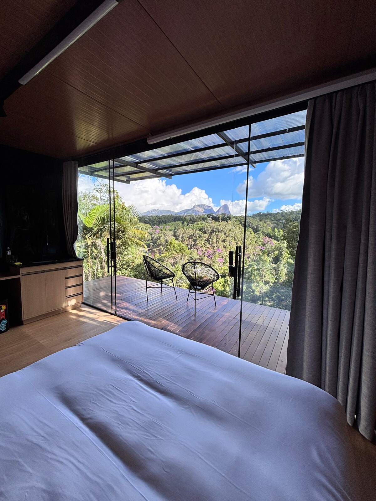 Cama com vidro panorâmico mostrando deck e Pedra Azul